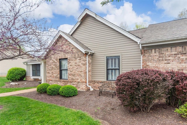 view of side of property featuring brick siding and roof with shingles