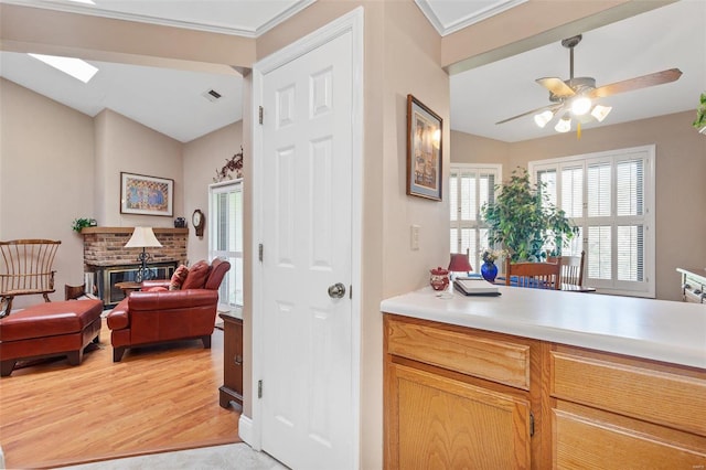 kitchen with light wood-type flooring, visible vents, a brick fireplace, light countertops, and a ceiling fan