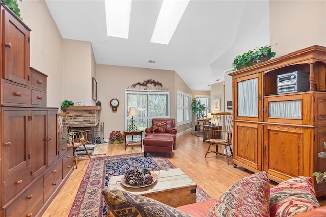 living area featuring light wood finished floors, visible vents, a fireplace, and vaulted ceiling with skylight