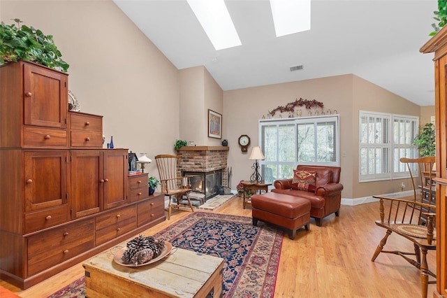 living room with light wood-style flooring, baseboards, lofted ceiling with skylight, visible vents, and a brick fireplace