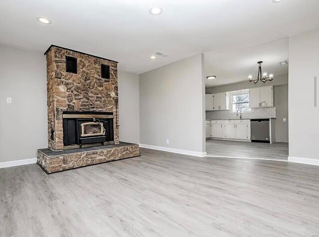 unfurnished living room with light wood finished floors, a sink, a notable chandelier, visible vents, and baseboards