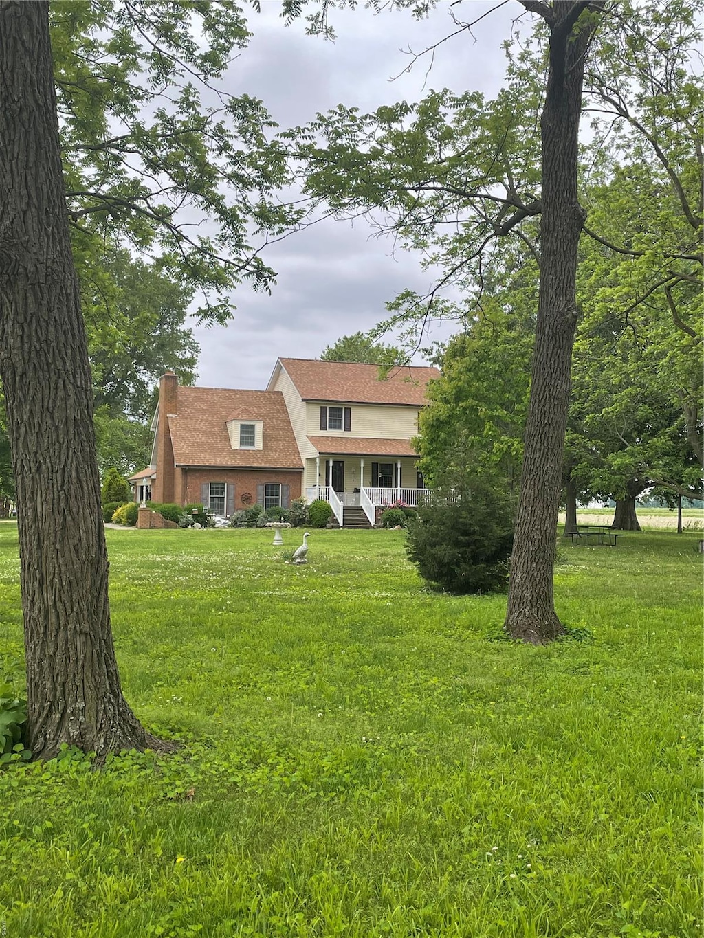 view of front facade with a front lawn, covered porch, stucco siding, and a chimney