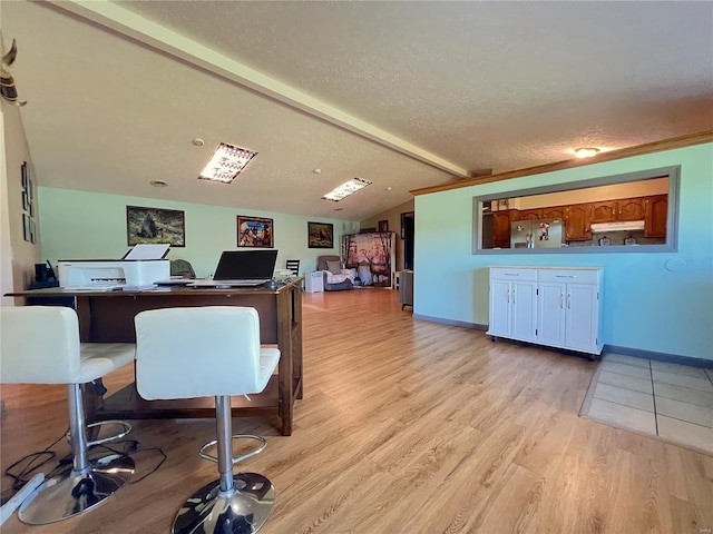 office space featuring light wood finished floors, a textured ceiling, baseboards, and vaulted ceiling with beams