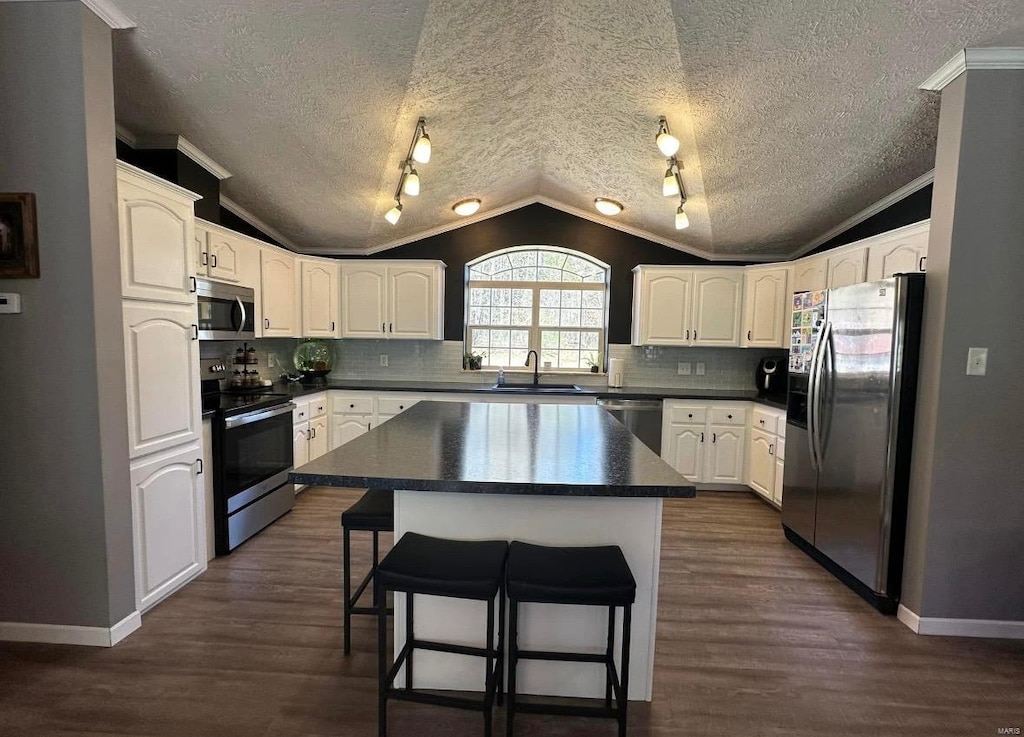 kitchen with a sink, stainless steel appliances, a breakfast bar area, vaulted ceiling, and dark countertops