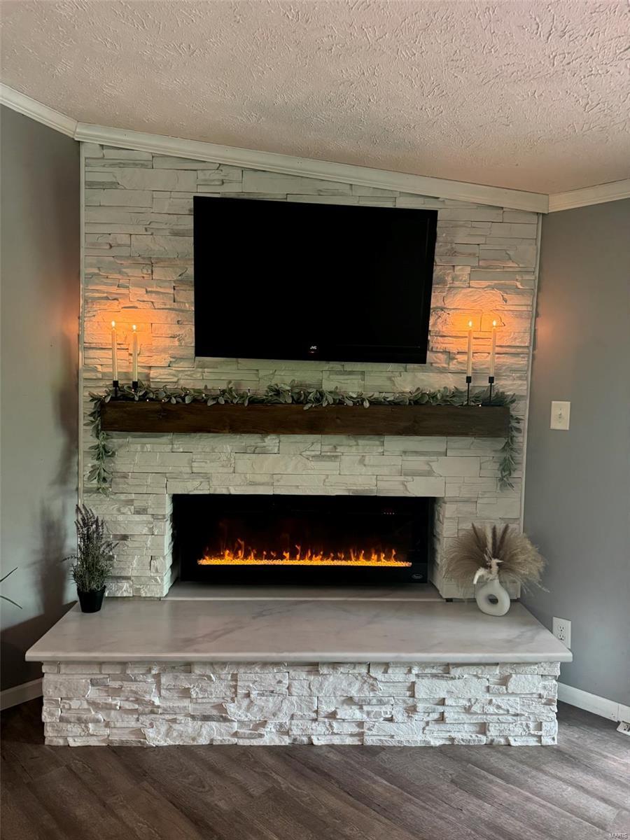 interior details featuring a textured ceiling, baseboards, crown molding, wood finished floors, and a fireplace