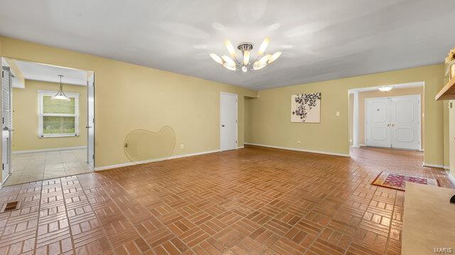 empty room featuring baseboards, visible vents, an inviting chandelier, and brick floor
