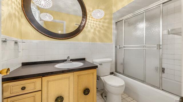 full bathroom featuring toilet, tile walls, vanity, tile patterned flooring, and enclosed tub / shower combo