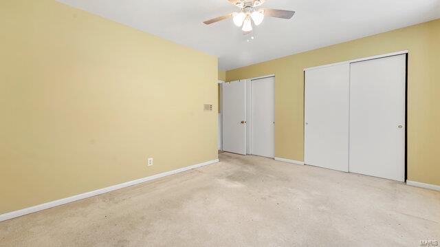 unfurnished bedroom featuring light colored carpet, two closets, baseboards, and ceiling fan