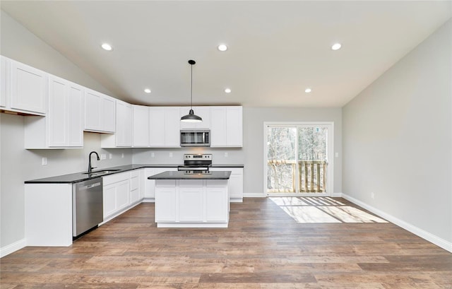 kitchen with a center island, a sink, dark countertops, white cabinets, and appliances with stainless steel finishes