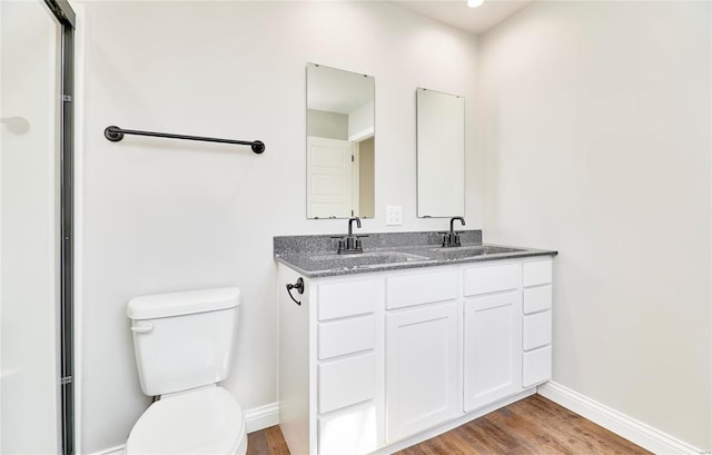 full bath with double vanity, toilet, wood finished floors, a sink, and baseboards