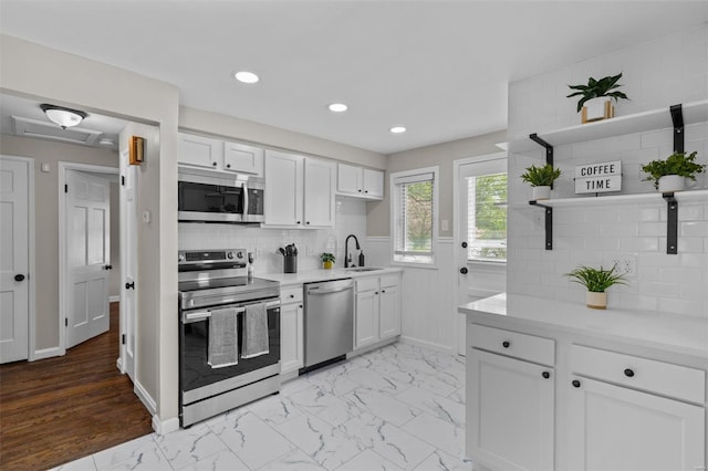 kitchen featuring light countertops, stainless steel appliances, open shelves, and a sink