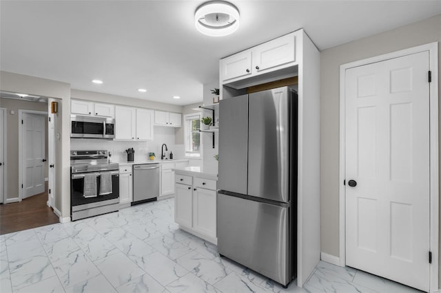 kitchen with a sink, stainless steel appliances, white cabinets, light countertops, and marble finish floor