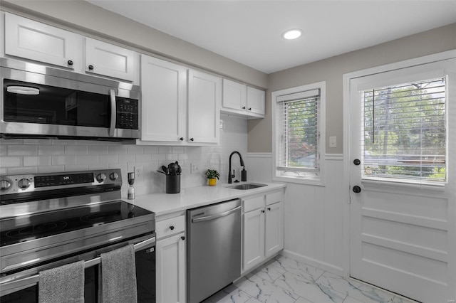 kitchen featuring a sink, white cabinetry, wainscoting, light countertops, and appliances with stainless steel finishes