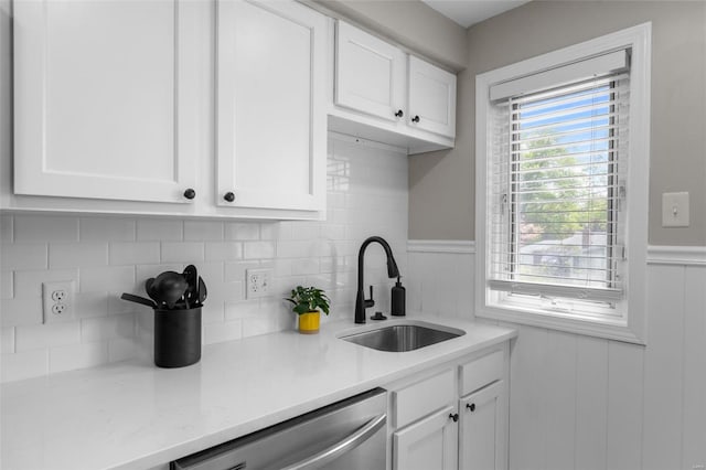 kitchen with a wainscoted wall, white cabinetry, stainless steel dishwasher, and a sink