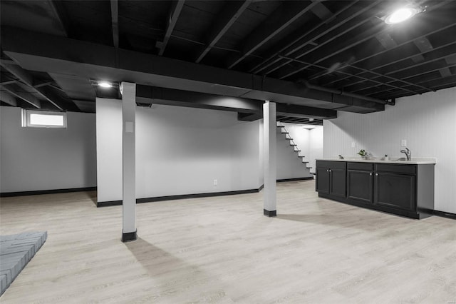 basement with light wood finished floors, baseboards, a sink, and stairs