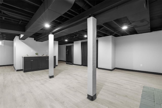 finished below grade area with light wood-style floors, baseboards, bar area, and black fridge