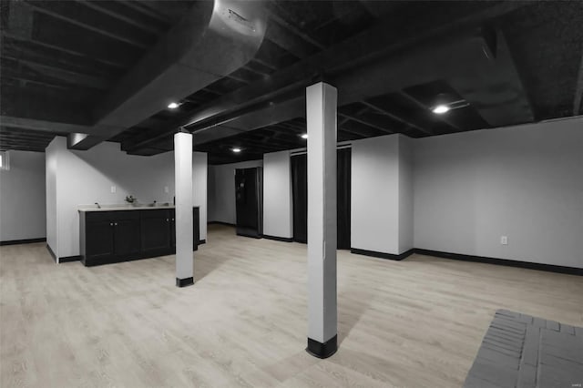 finished basement featuring indoor bar, baseboards, and light wood-type flooring