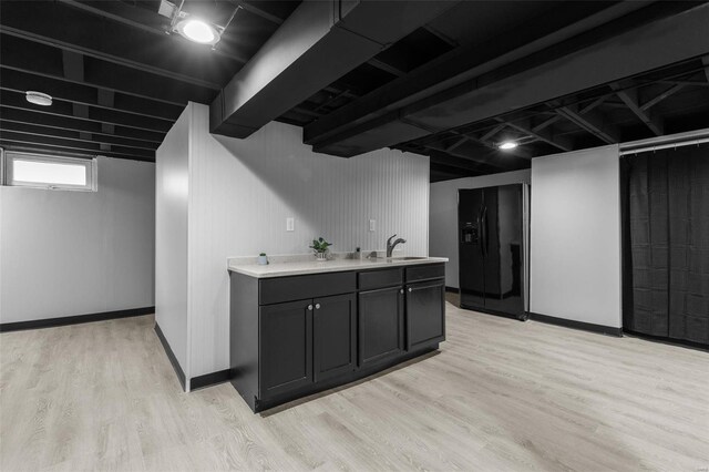 basement featuring light wood-style flooring, baseboards, a sink, and black refrigerator with ice dispenser