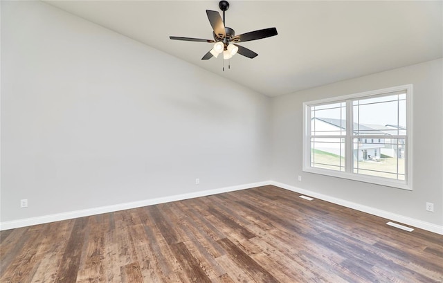 empty room featuring lofted ceiling, dark wood-type flooring, visible vents, a ceiling fan, and baseboards