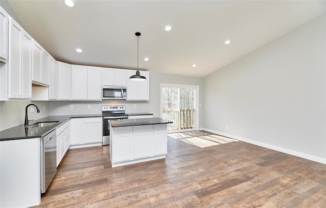 kitchen with a center island, light wood finished floors, a sink, dark countertops, and appliances with stainless steel finishes