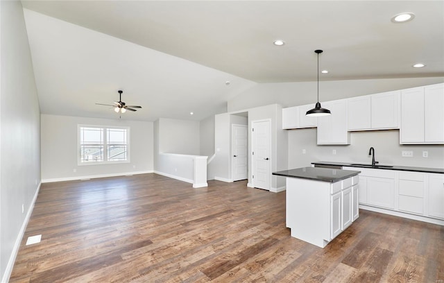 kitchen with a sink, vaulted ceiling, a center island, white cabinets, and dark countertops