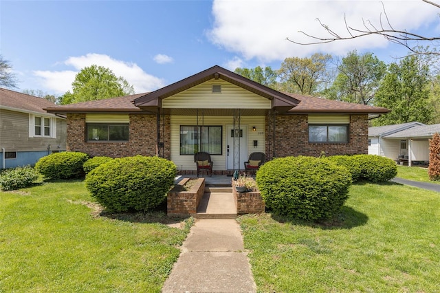 view of front facade featuring a front lawn, a shingled roof, brick siding, and a porch
