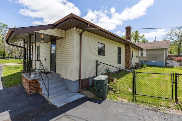 view of side of home featuring a gate, central AC, a chimney, fence, and a lawn