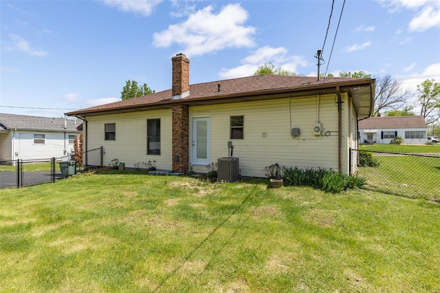 rear view of house with central air condition unit, a chimney, fence, and a lawn