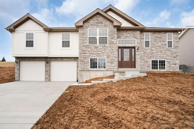 bi-level home with concrete driveway, stone siding, an attached garage, and board and batten siding