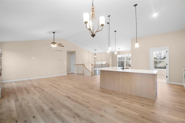 kitchen with lofted ceiling, ceiling fan with notable chandelier, open floor plan, light wood-style floors, and an island with sink