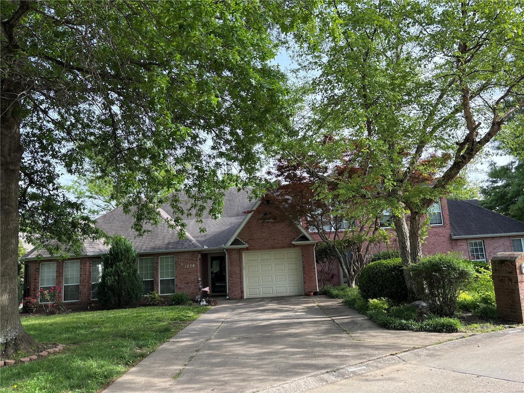 view of front of property with brick siding, an attached garage, concrete driveway, and a front yard