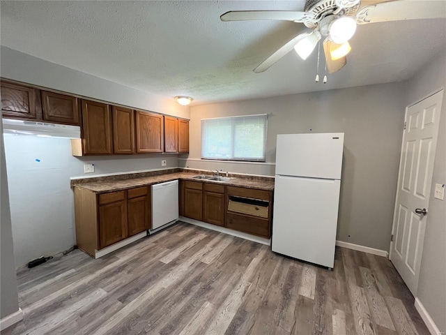 kitchen with light wood finished floors, brown cabinets, a sink, dark countertops, and white appliances