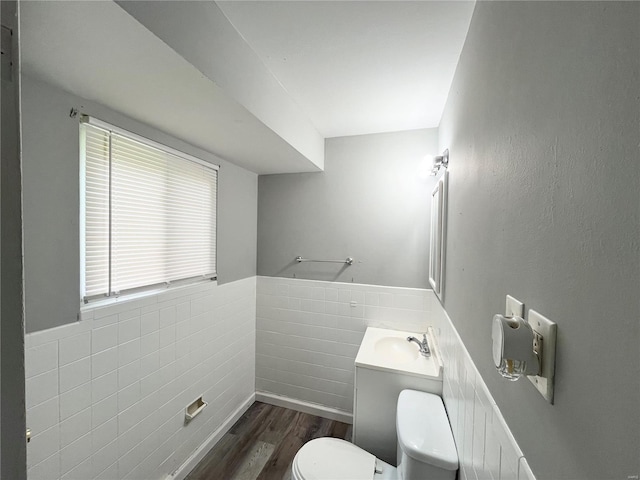 half bathroom with a sink, toilet, tile walls, a wainscoted wall, and wood finished floors