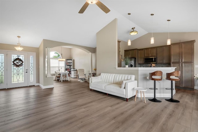 living room with wood finished floors, a ceiling fan, high vaulted ceiling, baseboards, and arched walkways