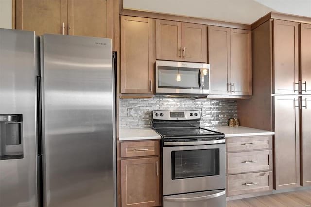 kitchen featuring stainless steel appliances, tasteful backsplash, light countertops, and light wood-style flooring