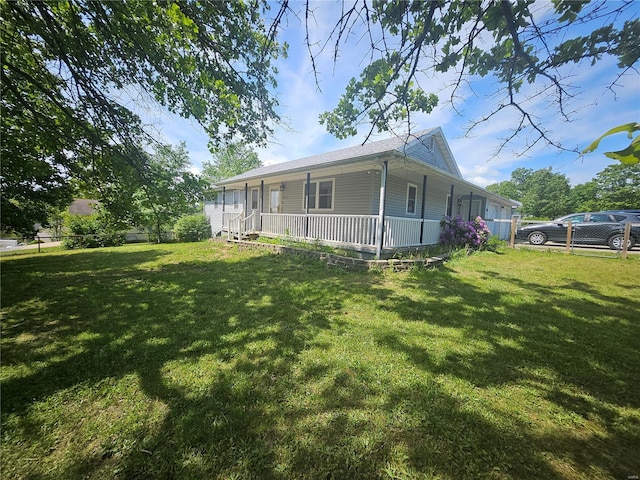 view of side of property featuring covered porch, fence, and a lawn