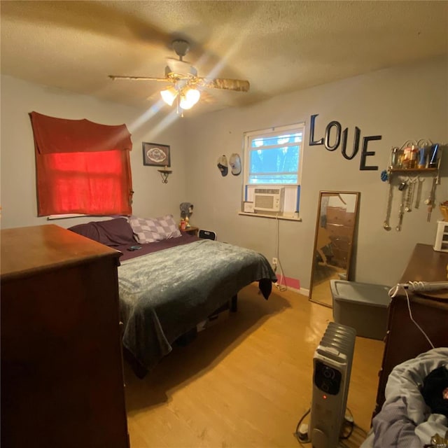 bedroom featuring cooling unit, a textured ceiling, light wood finished floors, and a ceiling fan