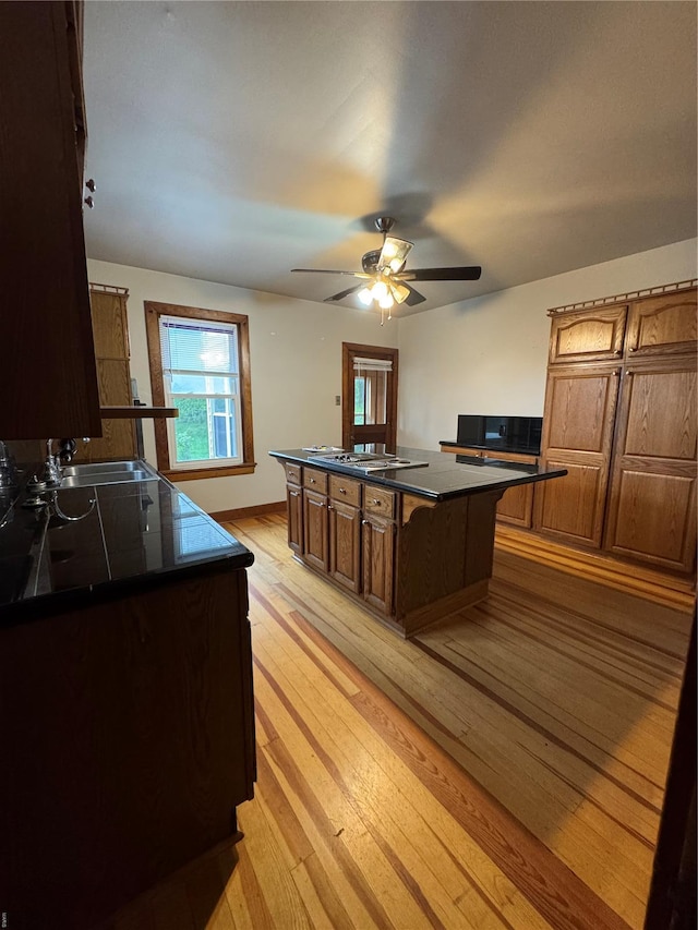 kitchen with a sink, light wood-style flooring, a center island, cooktop, and dark countertops