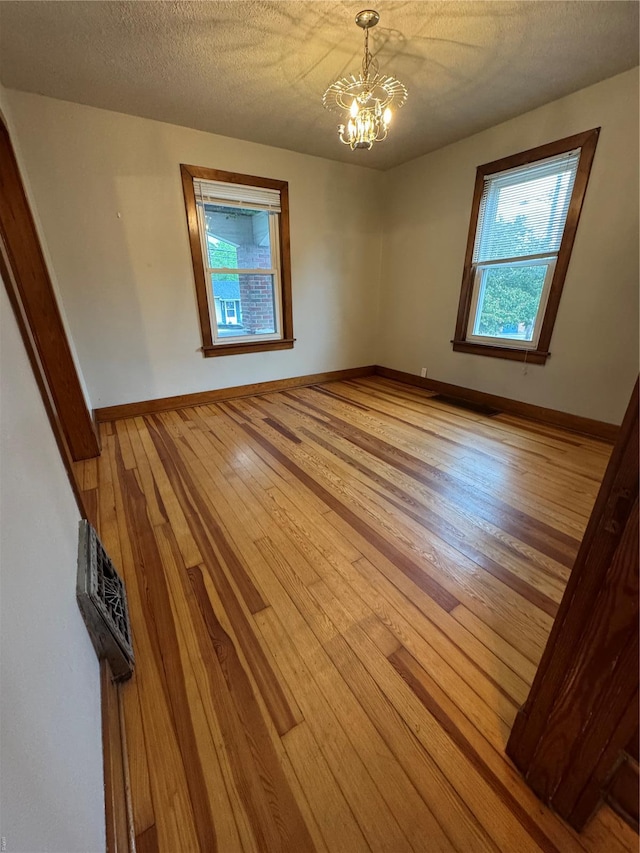 unfurnished room featuring a textured ceiling, baseboards, wood-type flooring, and a notable chandelier