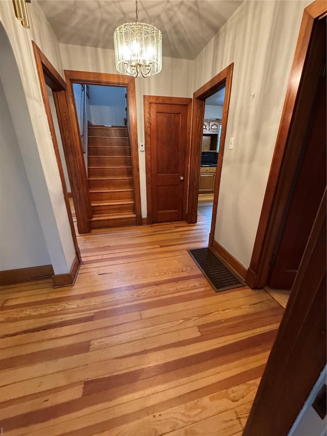 hallway with light wood finished floors, visible vents, baseboards, and a chandelier