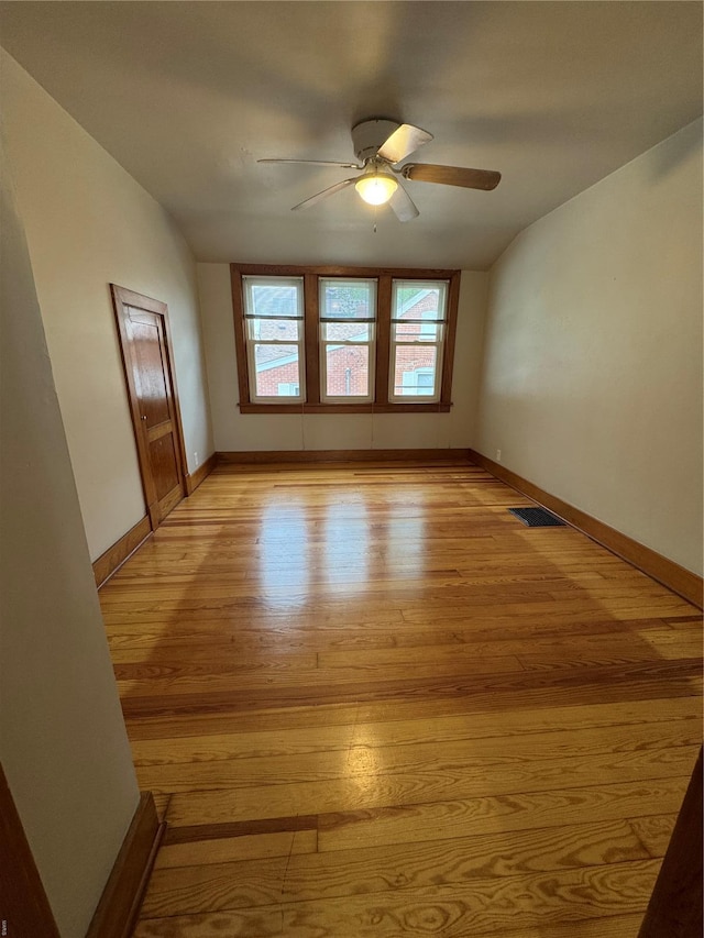 spare room featuring lofted ceiling, visible vents, light wood-style flooring, a ceiling fan, and baseboards