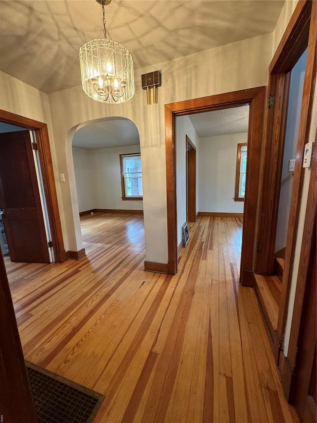 hall featuring light wood finished floors, a wealth of natural light, arched walkways, and a notable chandelier