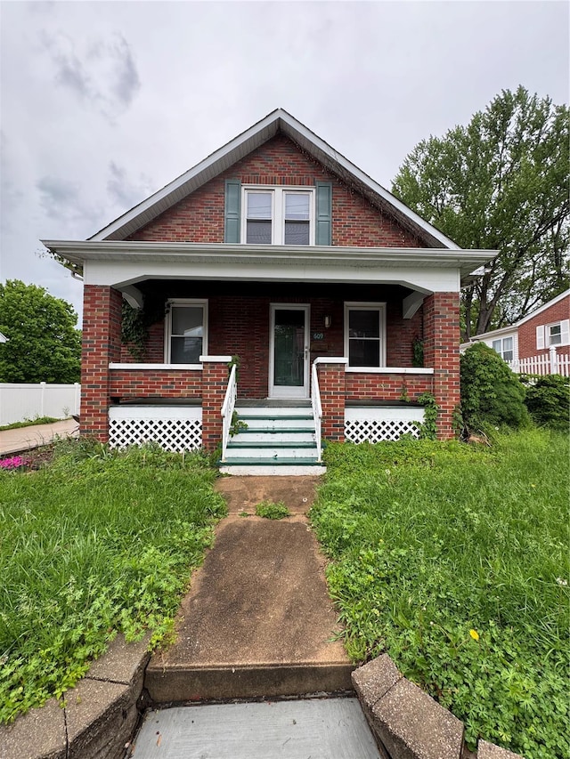 bungalow featuring brick siding, covered porch, and fence