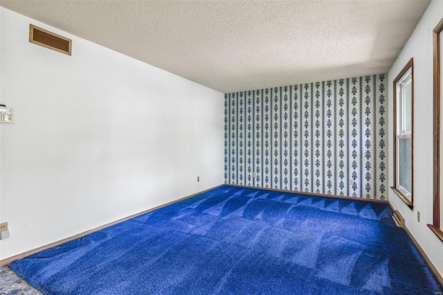 spare room featuring carpet floors, a textured ceiling, and wallpapered walls