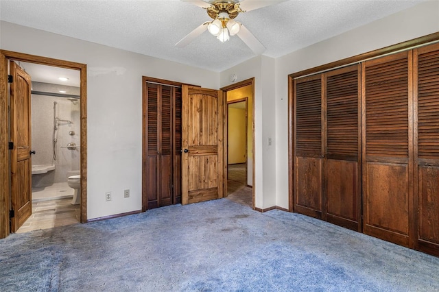 unfurnished bedroom featuring carpet flooring, baseboards, ensuite bathroom, a ceiling fan, and a textured ceiling