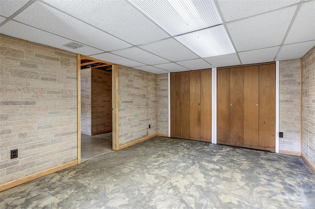 finished below grade area with a drop ceiling, baseboards, and brick wall