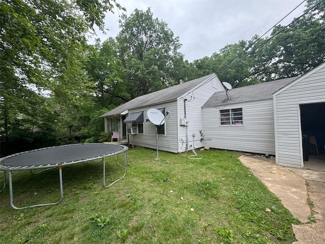 back of property with a trampoline, a lawn, and roof with shingles