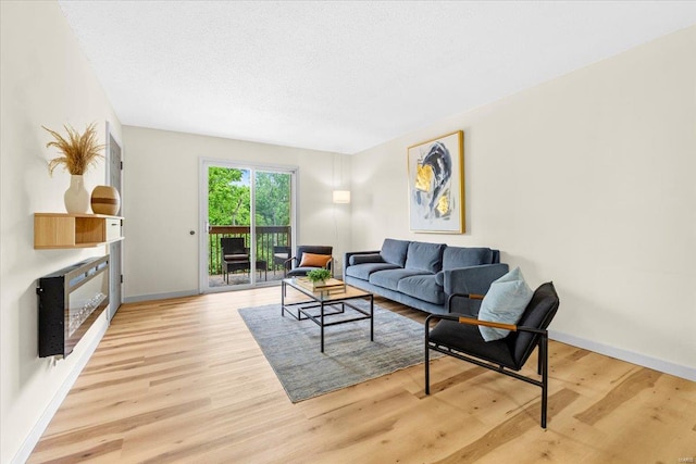living room with a glass covered fireplace, light wood-style floors, baseboards, and a textured ceiling