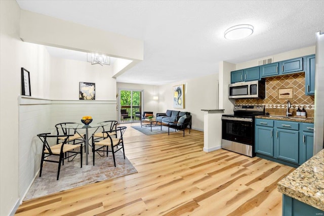 kitchen with appliances with stainless steel finishes, blue cabinets, light wood finished floors, and backsplash