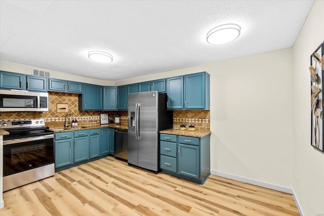 kitchen featuring appliances with stainless steel finishes, light wood-style flooring, blue cabinetry, a sink, and a textured ceiling